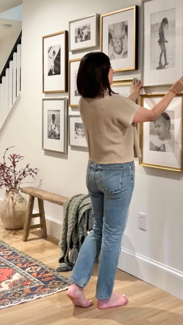 Woman arranging a gallery wall of framed black and white photos in a living room