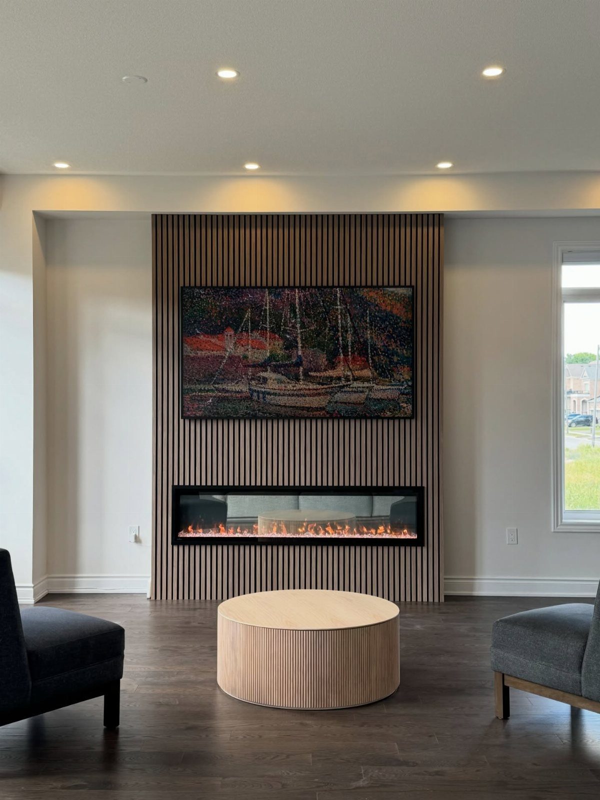 Large painting of sailboats hanging above a modern linear fireplace on wood-slat wall.