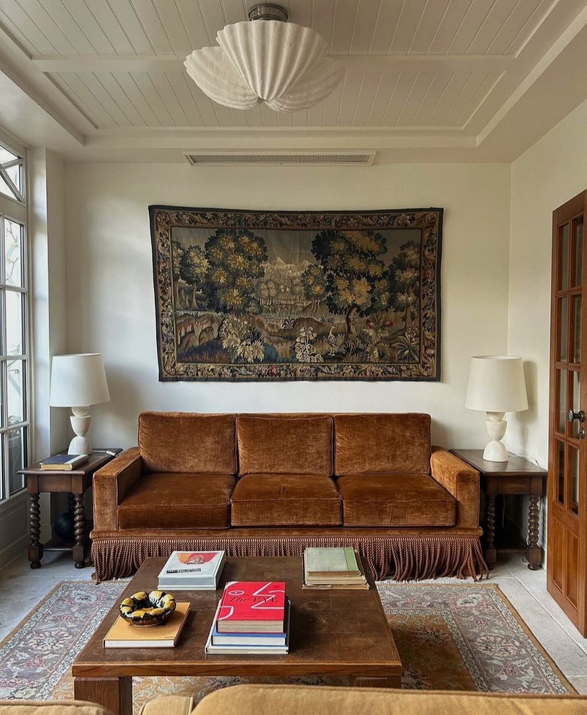Large woven landscape tapestry hanging on a white wall above a brown velvet sofa