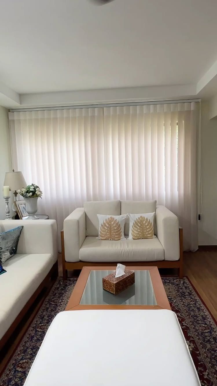 White vertical blinds covering a large window in a bright living room.