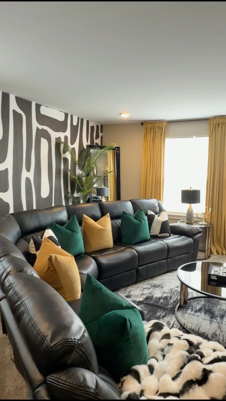 Black leather sectional sofa with colorful pillows against a patterned accent wall.