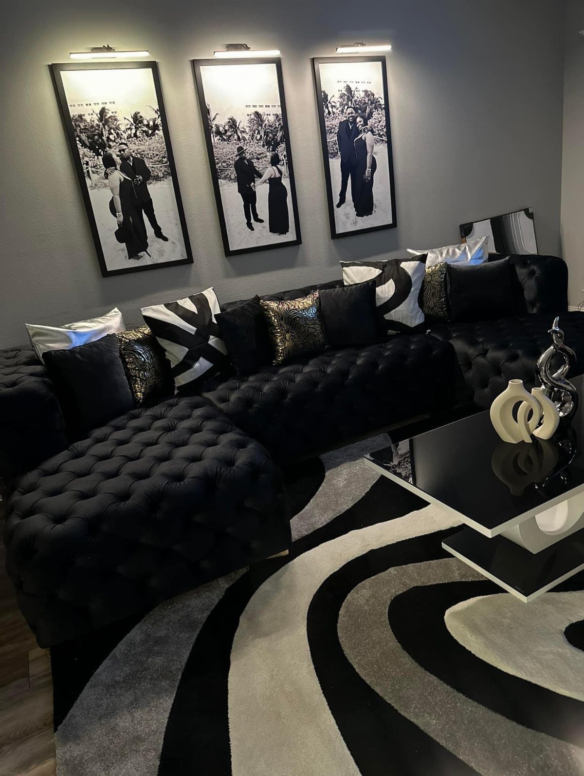 Tufted black sectional sofa with decorative pillows and a swirl patterned rug.