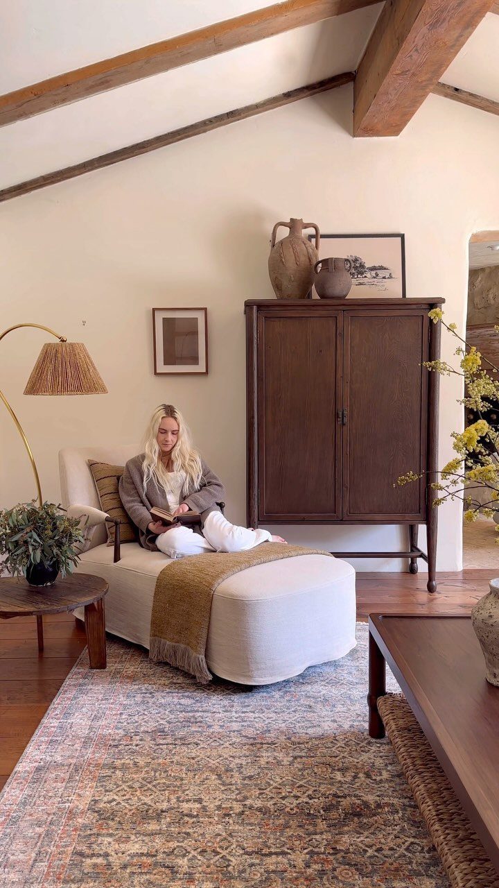 Woman reading on a white chaise lounge in a styled living room with rug.