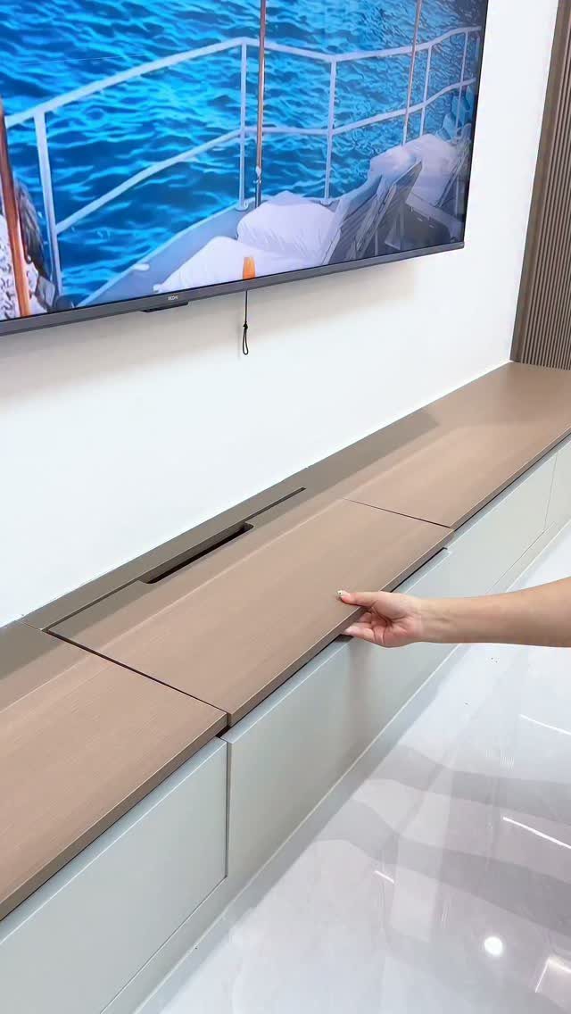 Wooden TV console with a hidden storage compartment being opened by a hand.