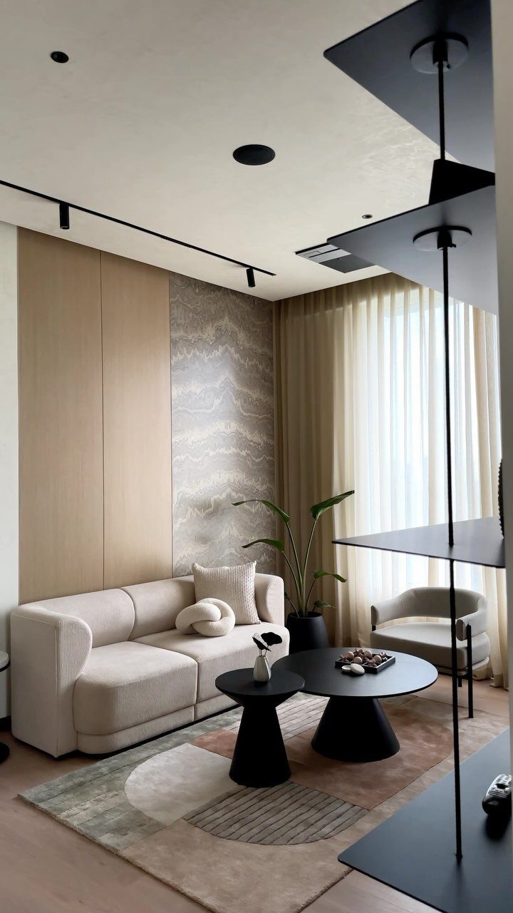 Modern lounge room with a cream sofa, black tables, and a patterned rug.