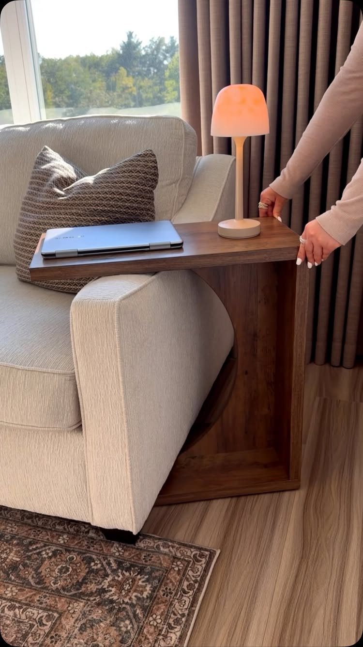 Wooden C-shaped side table with a lamp and laptop next to a beige sofa.