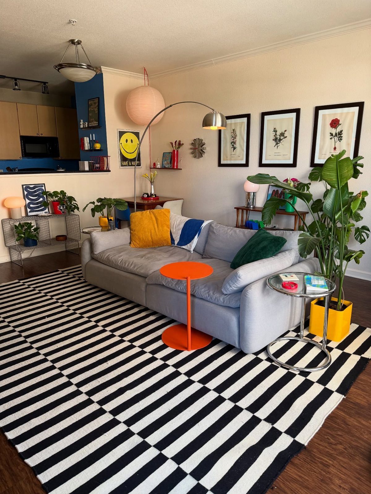 Grey sofa with colorful pillows and an orange table on a striped rug.