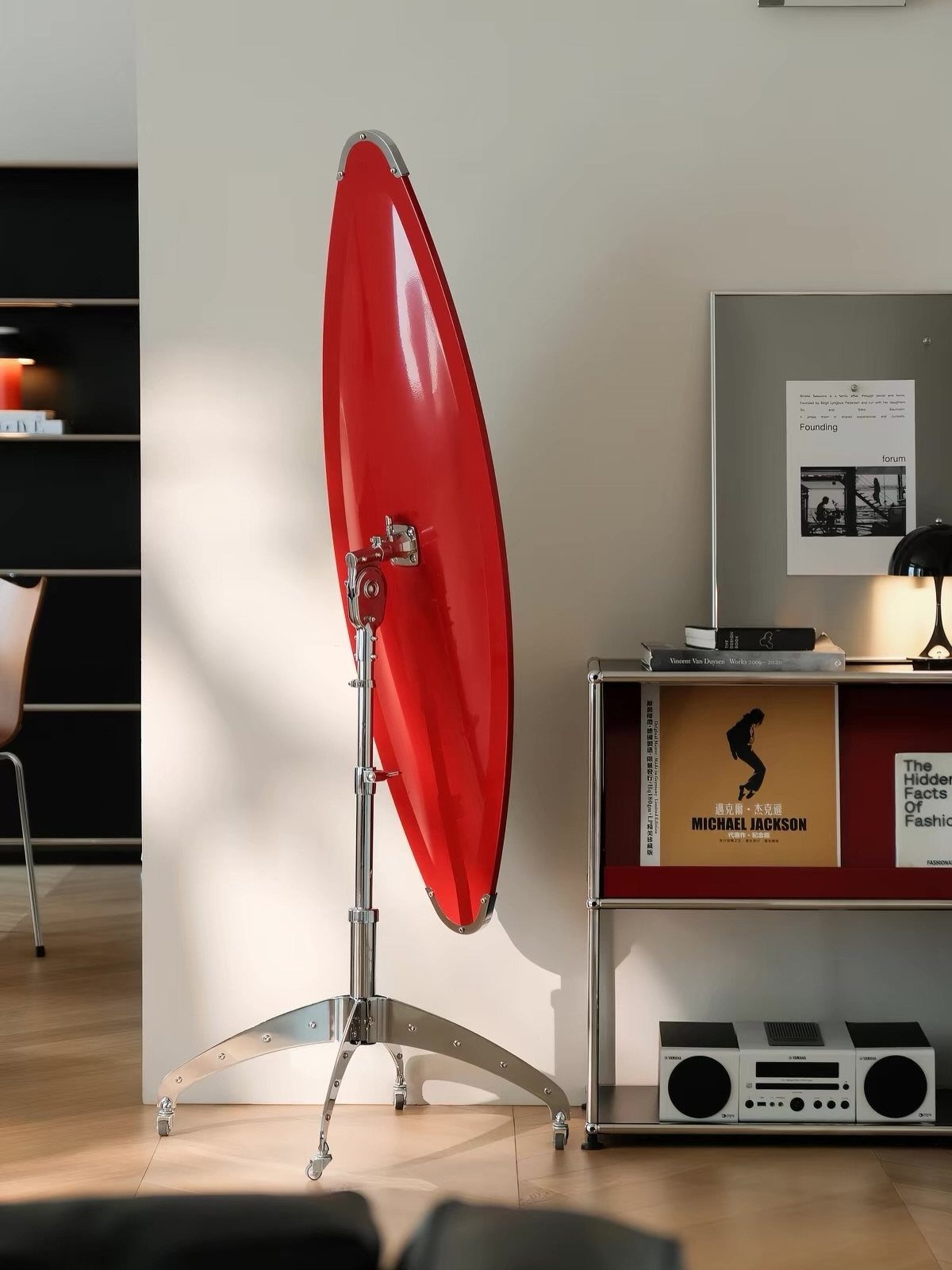 Large circular red mirror on a chrome tripod stand in a modern interior.