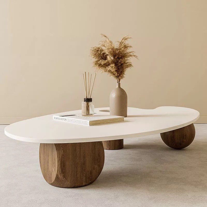 Organic white coffee table with wooden legs holding a vase and dried grass.
