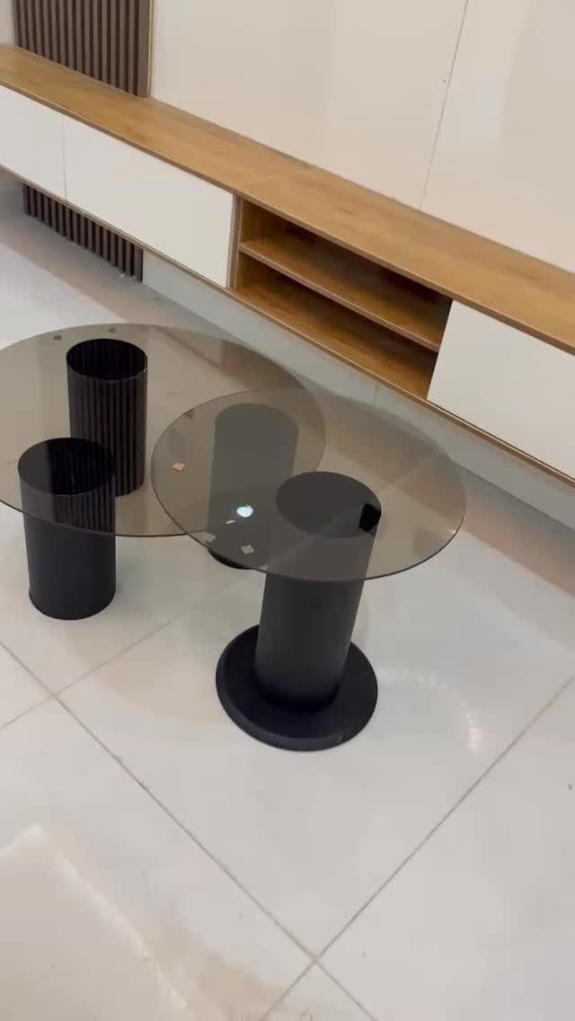 Two circular glass coffee tables with black cylindrical legs on white tiled flooring.