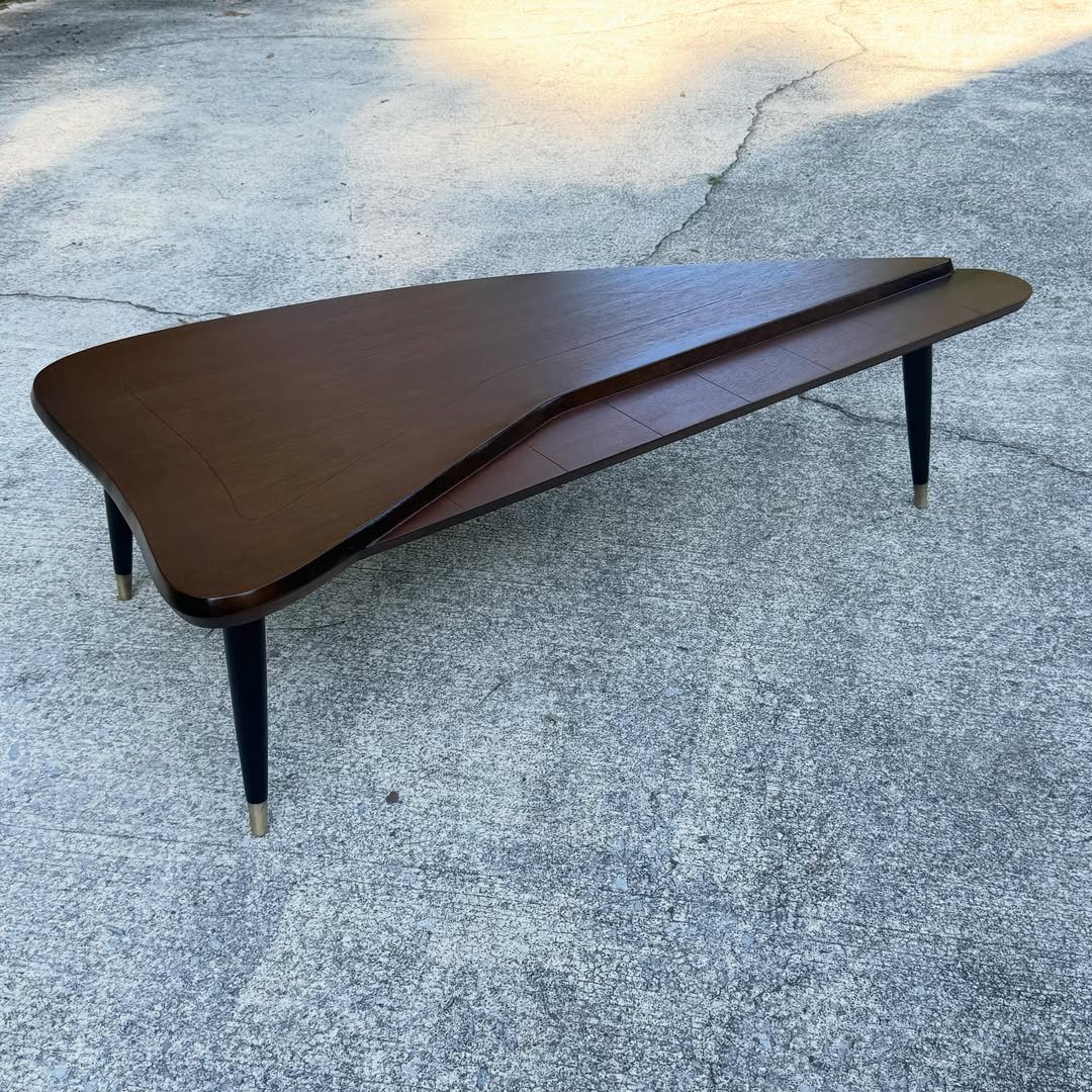 Mid-century modern dark wood coffee table with an asymmetrical shape on concrete.