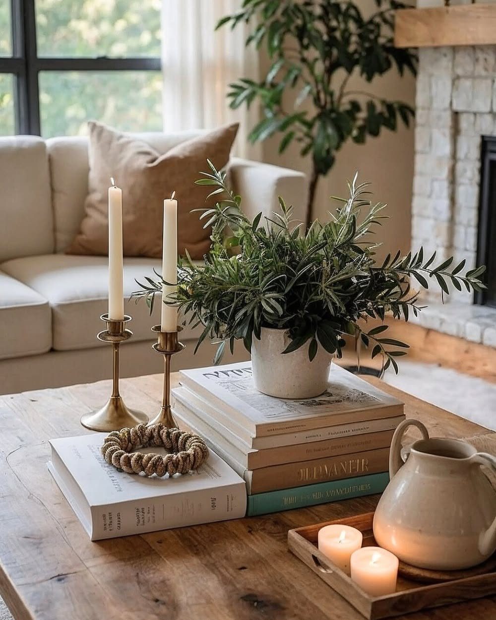 Wooden coffee table styled with a potted green plant, books, and white candles.