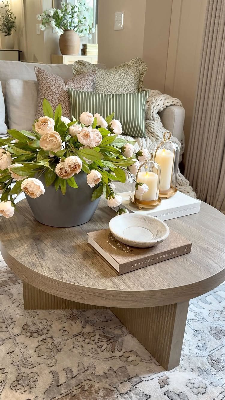 Round wooden coffee table with peach roses, lit candles, and stacked books.