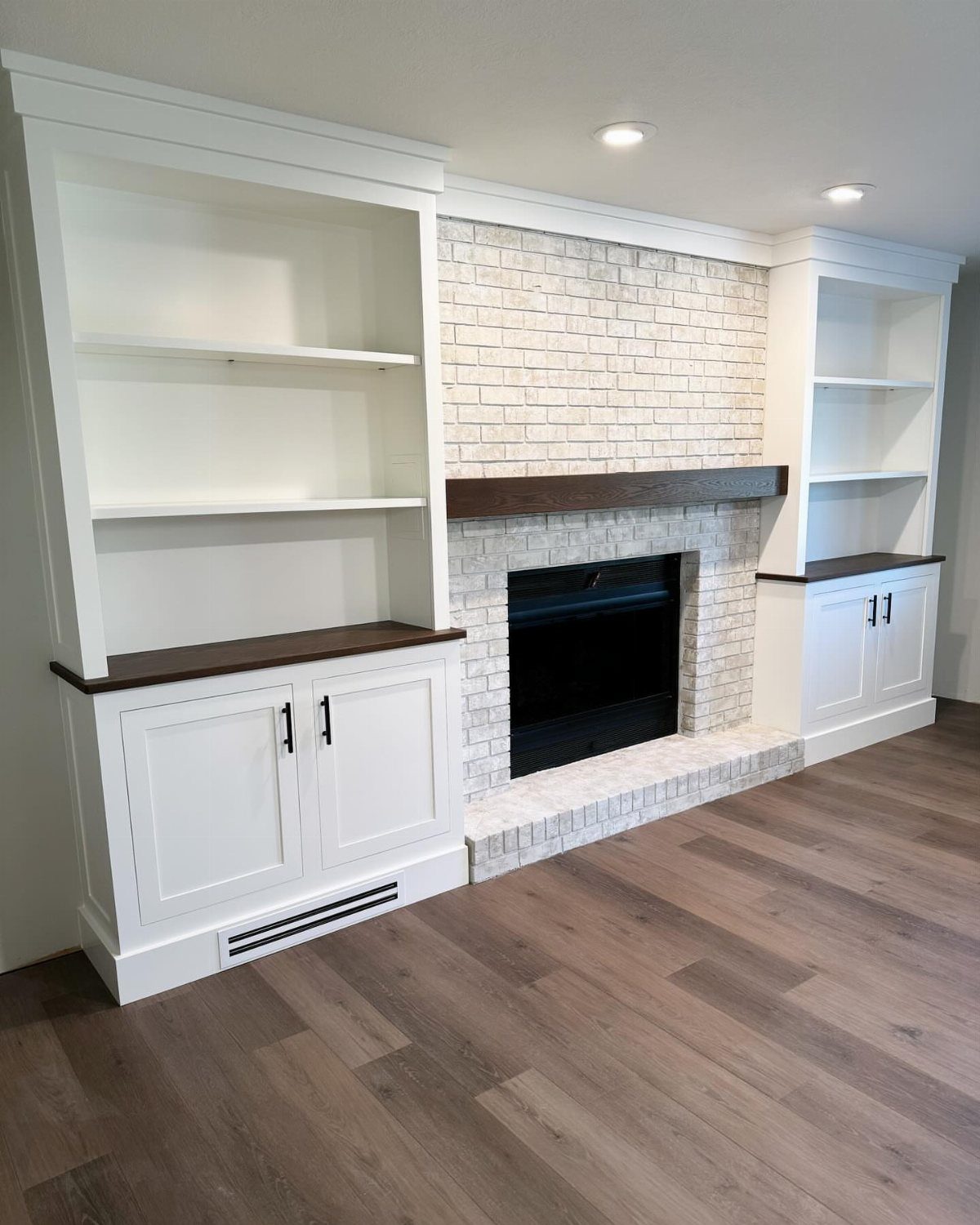 White built-in shelving units flanking a white brick fireplace with wood flooring.