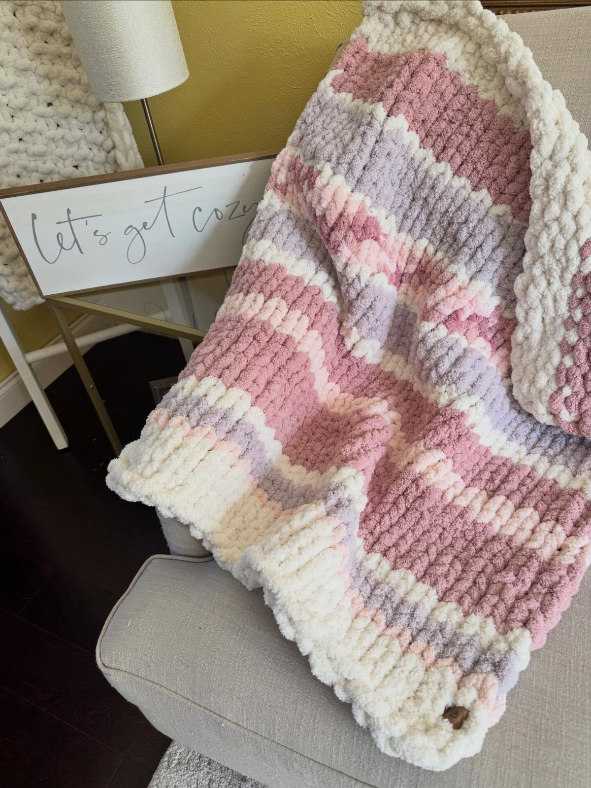 Chunky knit blanket with pink and purple stripes draped over a grey chair.