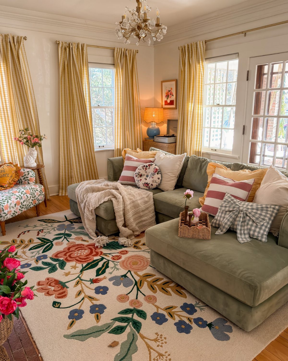 Green sectional sofa with colorful patterned pillows on a large floral area rug.