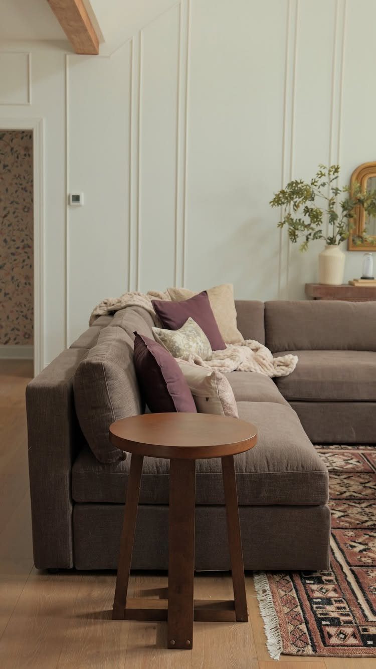 Grey sectional sofa with purple pillows and a round wooden side table.
