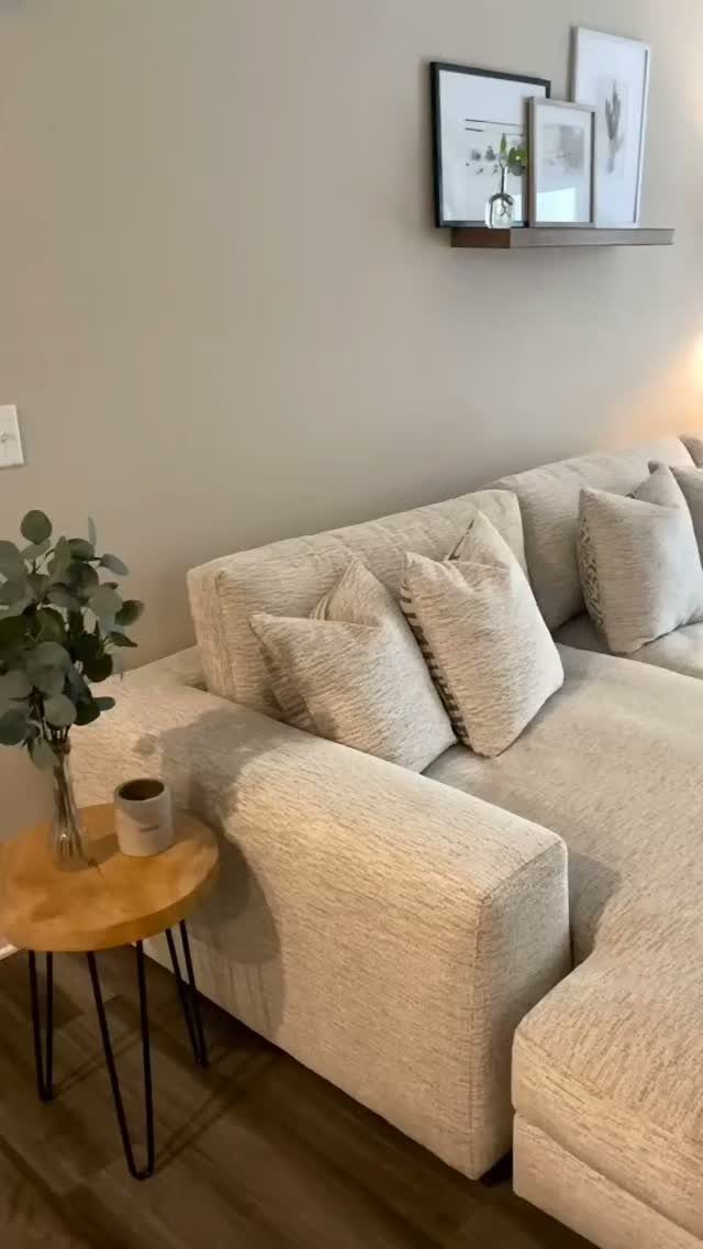 Beige sectional sofa with throw pillows and a small wooden side table.