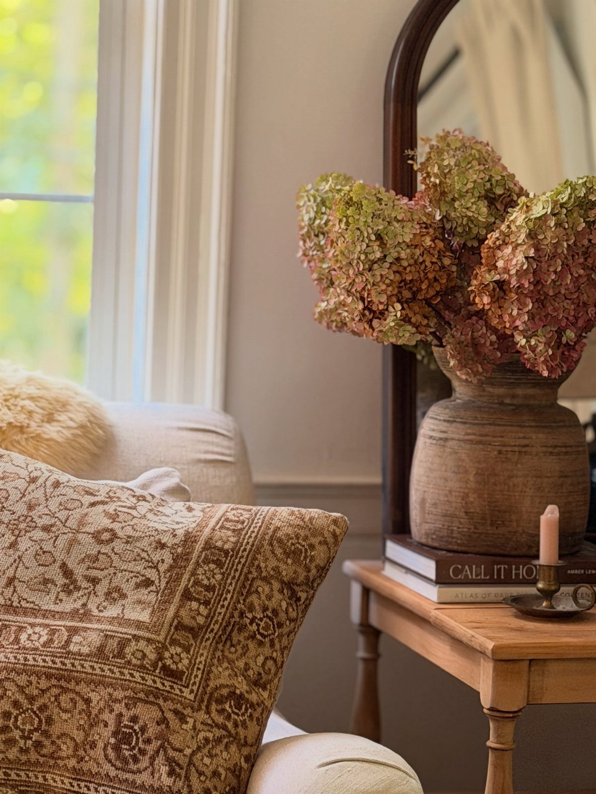Patterned brown pillow and rustic clay vase with dried flowers on wooden table.