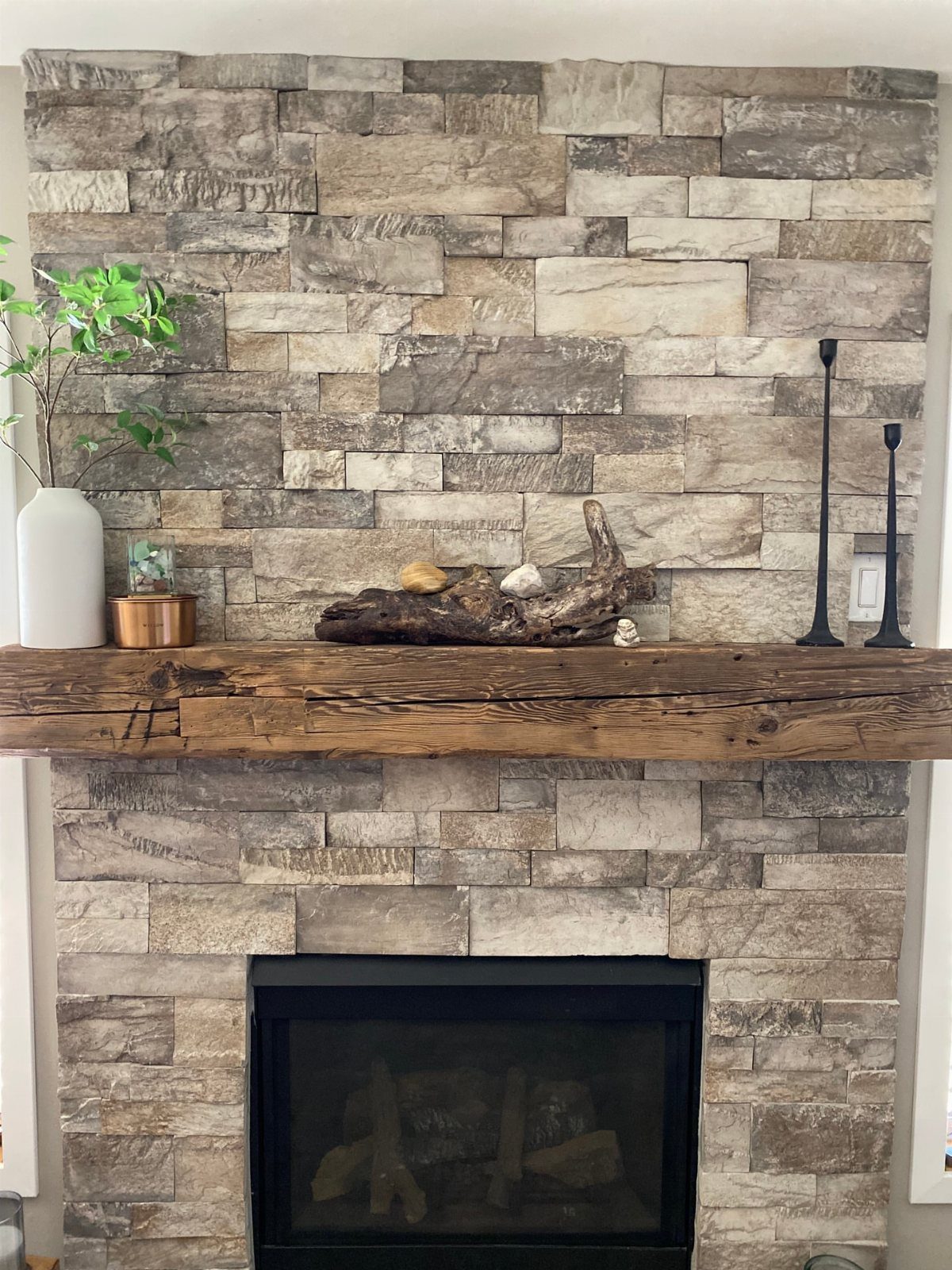 Rustic reclaimed wood mantel over a stacked stone fireplace with simple decor.