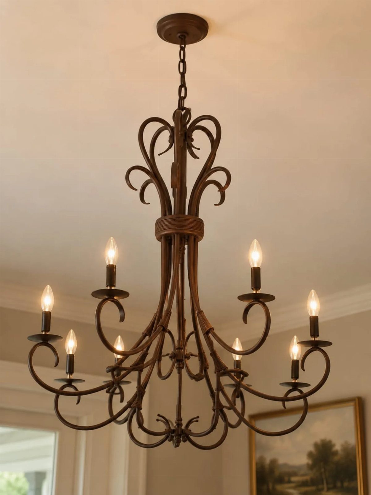 Wrought iron chandelier with curved arms and candle bulbs hanging from white ceiling