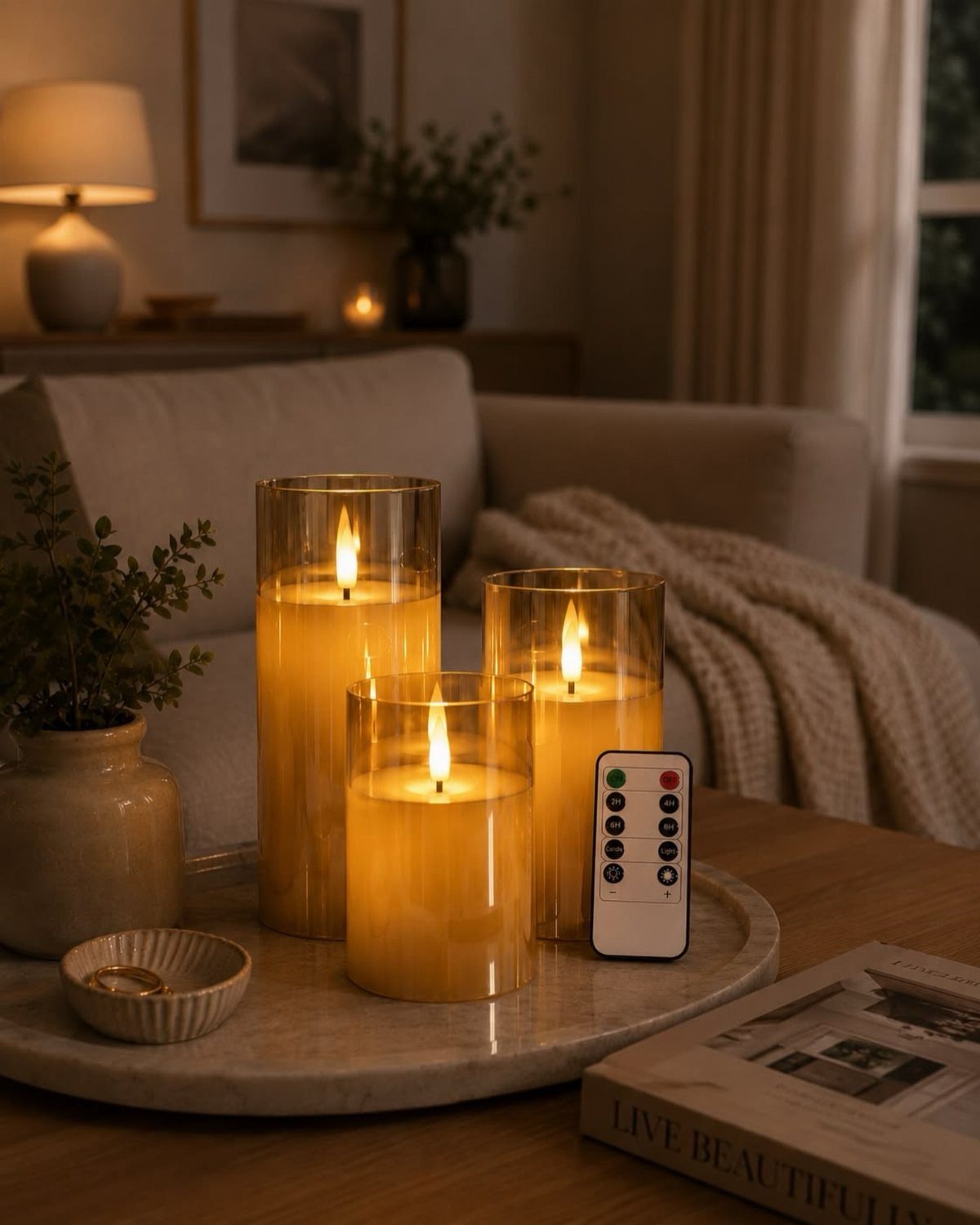 Three glowing pillar candles in glass holders on a marble tray in a living room