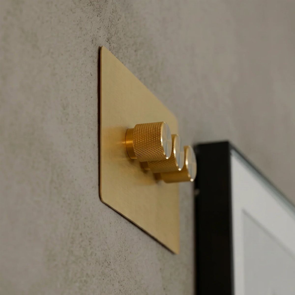 Gold rotary dimmer switches on a grey concrete wall next to a frame