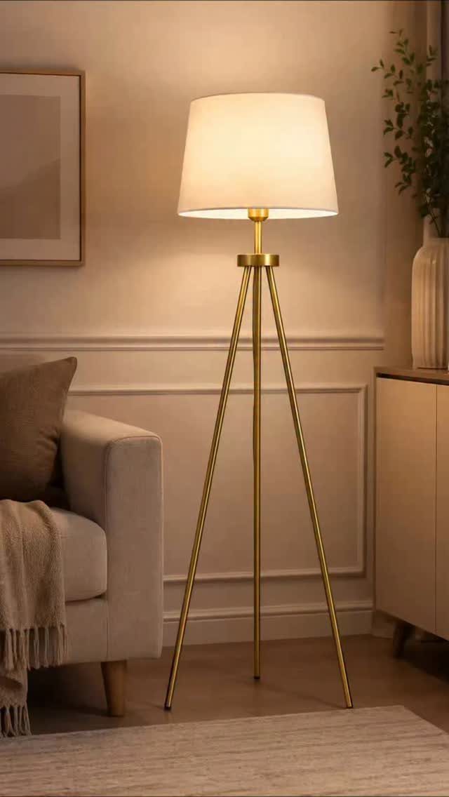 Gold tripod floor lamp with white shade illuminating a modern living room corner.