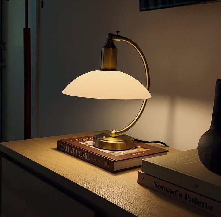 Gold table lamp with white dome shade illuminating books on a wooden surface