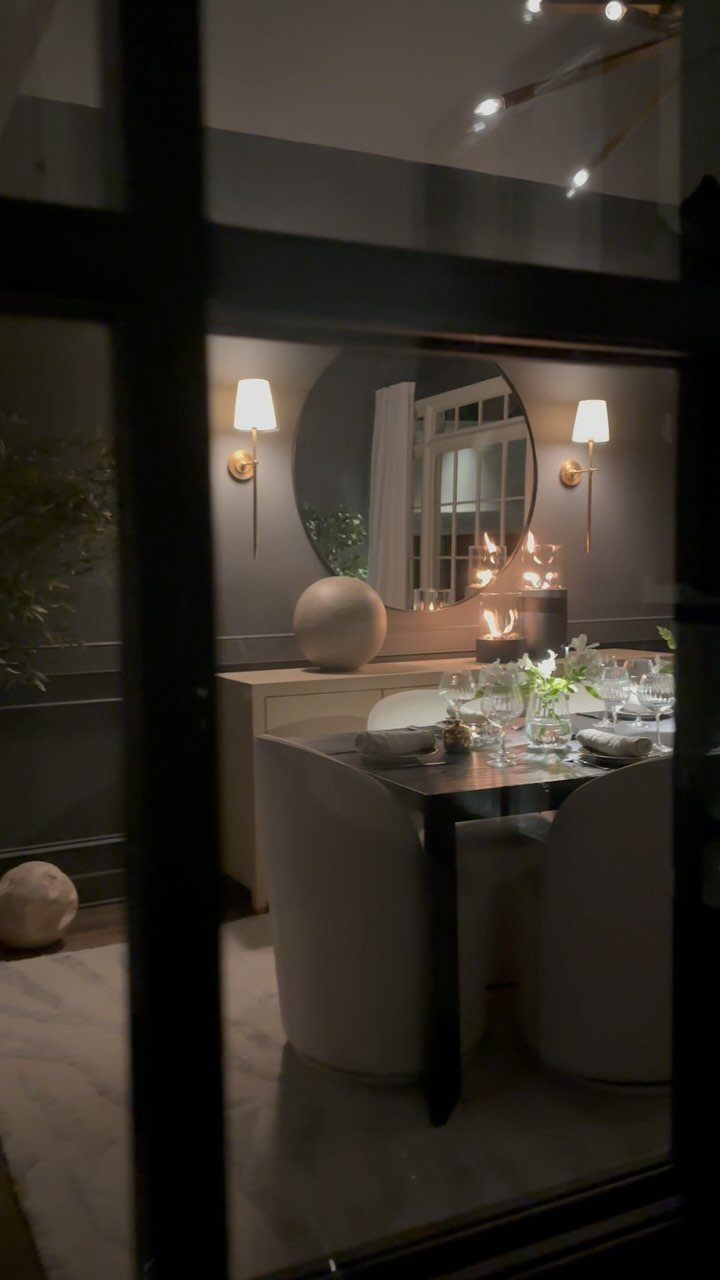 Two gold wall sconces with white shades flanking a round mirror in dining room