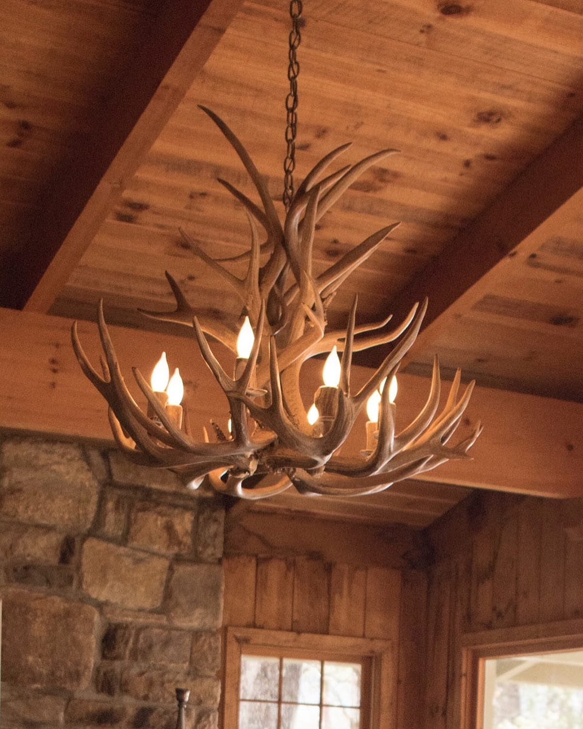 Antler chandelier with glowing lights hanging from a rustic wooden beamed ceiling.