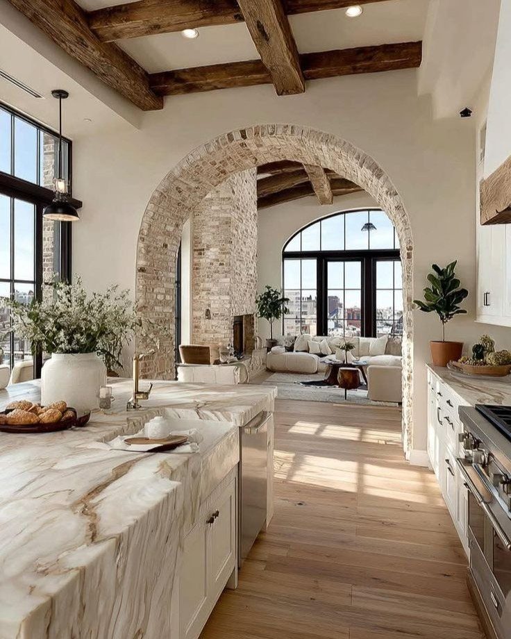 Kitchen with marble counters looking through a brick arch into a rustic living room.