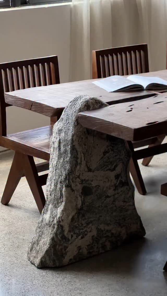 Wooden table with a live edge supported by a large natural stone base.