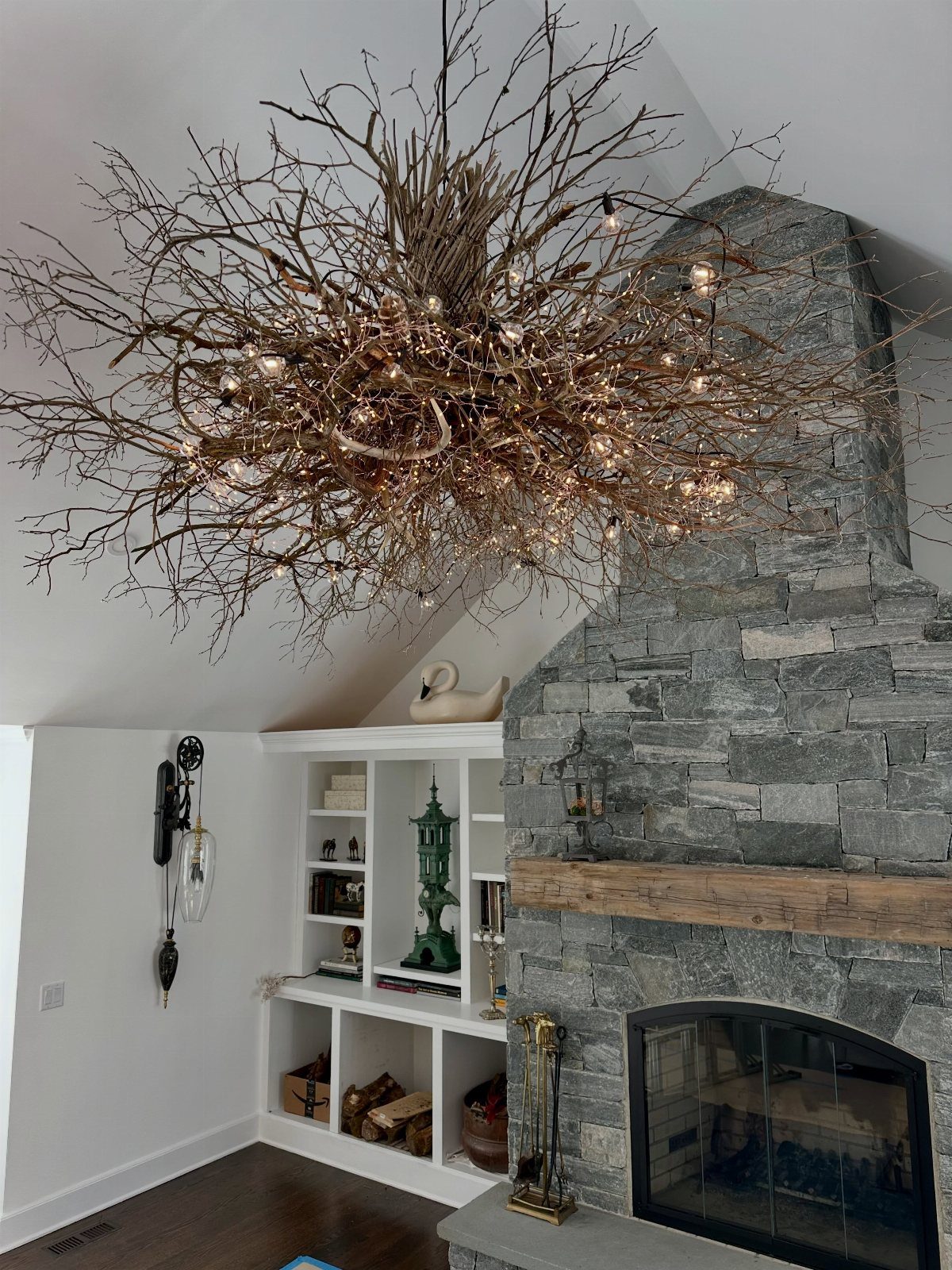 Stone fireplace and white shelving under a large branch chandelier in a living room