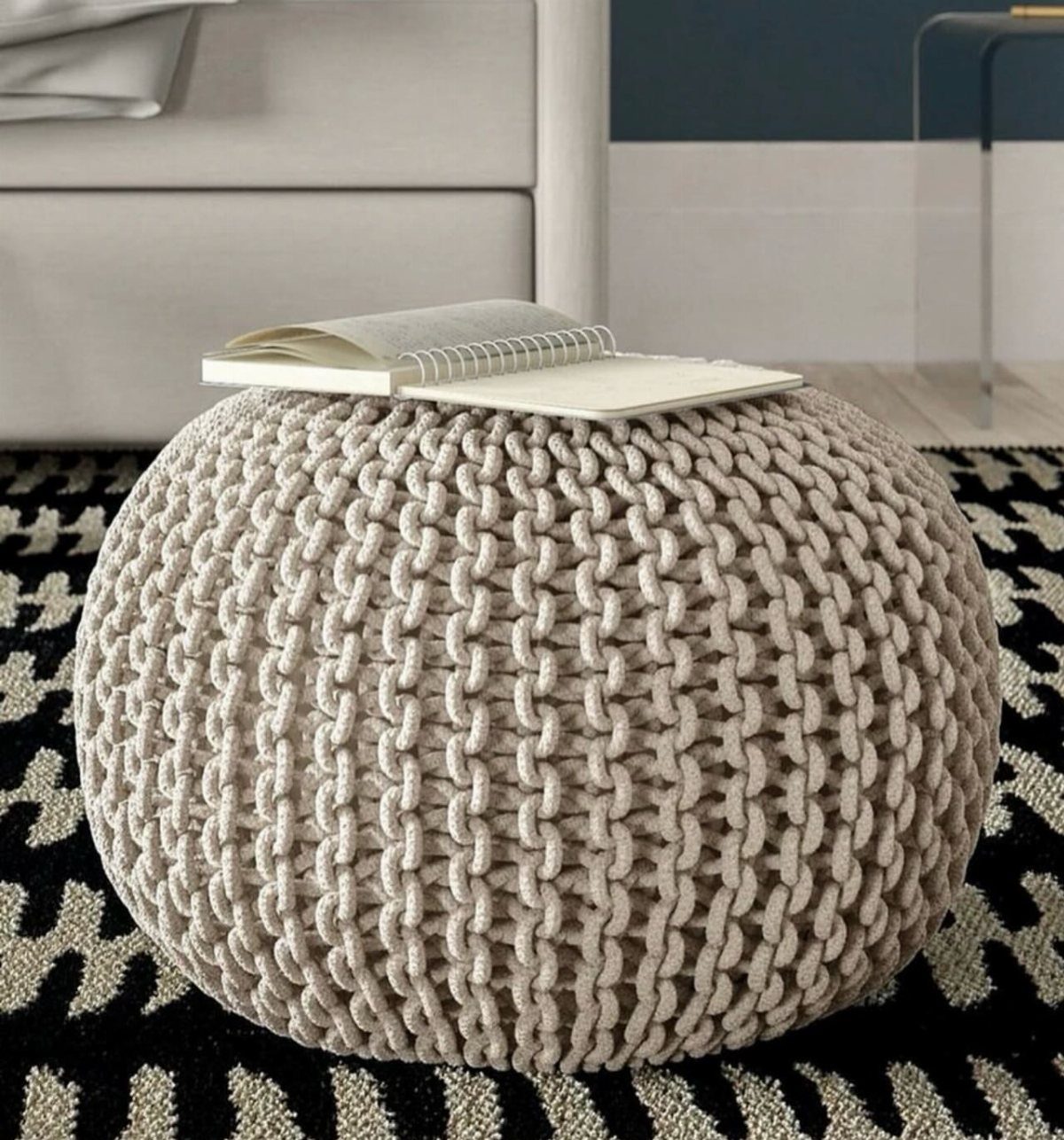 Beige chunky knit pouf with an open notebook on a patterned rug.