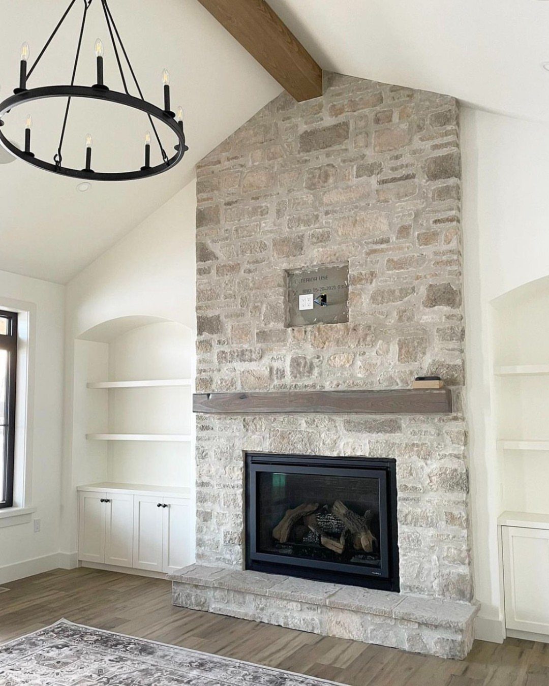 Stone fireplace with wooden mantel and black insert in a modern rustic room.