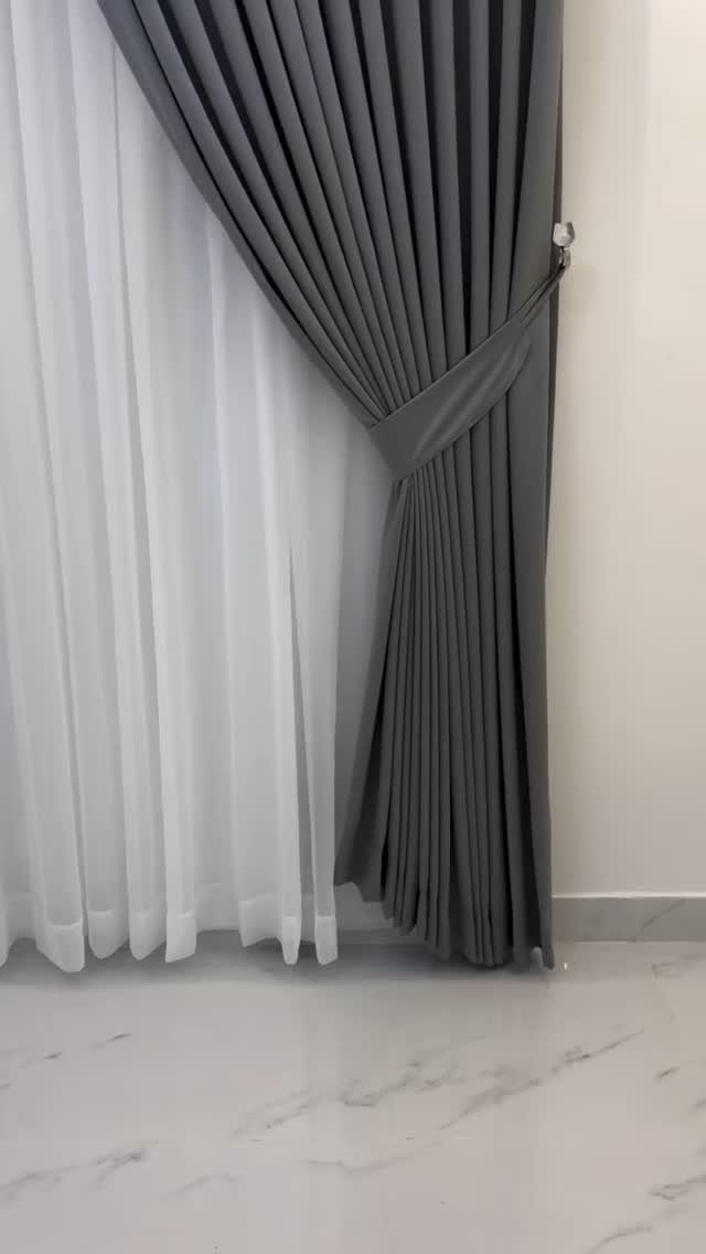Grey and white curtains draped in a room with white marble flooring.
