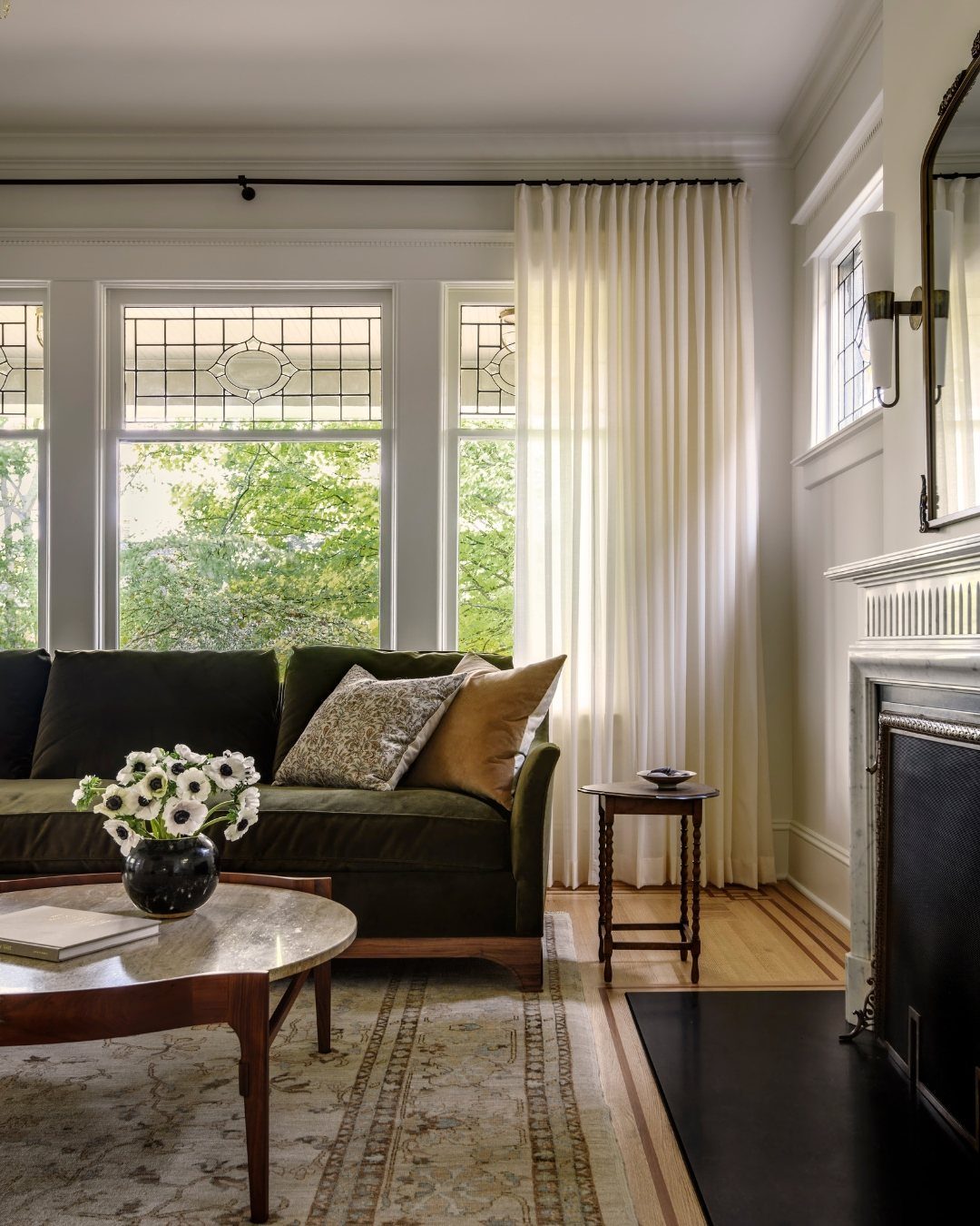 White floor-to-ceiling curtains in a living room with a green velvet sofa.