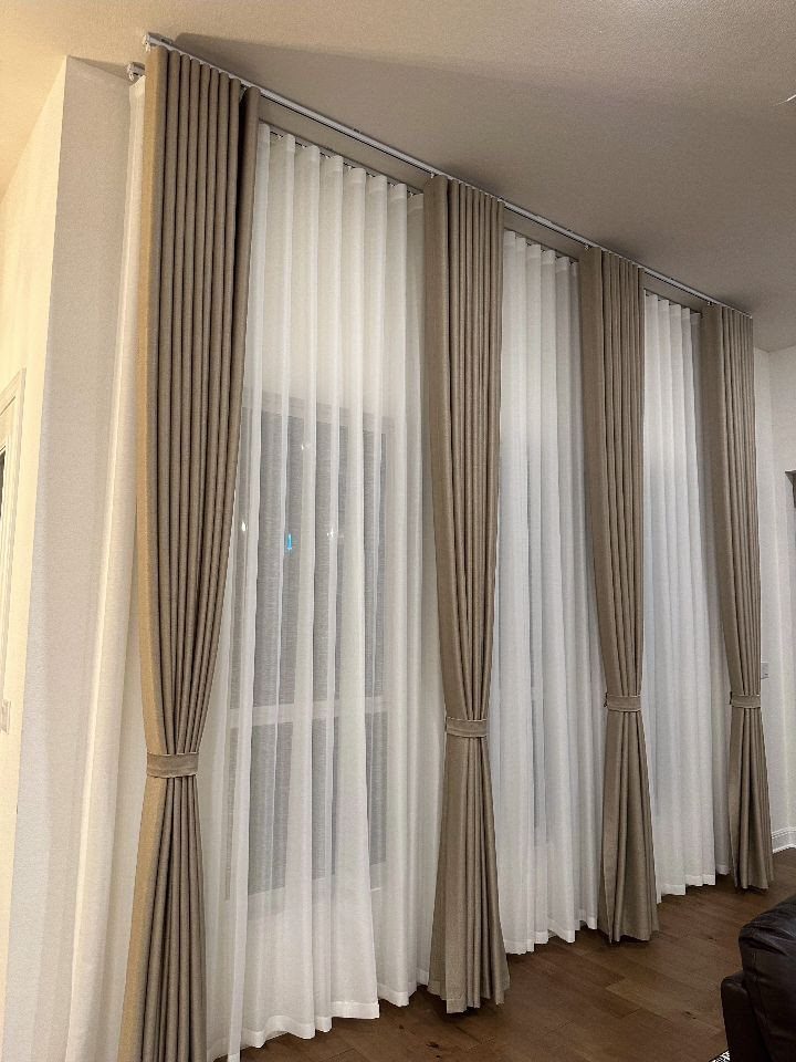 Taupe drapes tied back over white sheer panels in a modern living room.