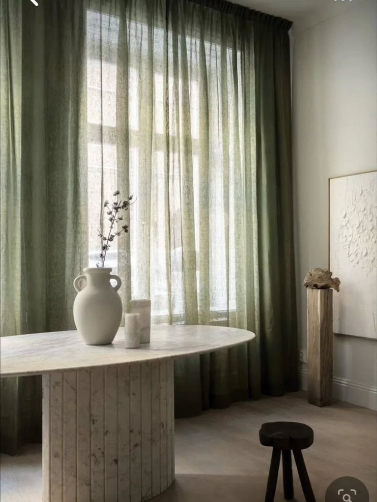 Green linen curtains in a modern room with a marble table and vase.
