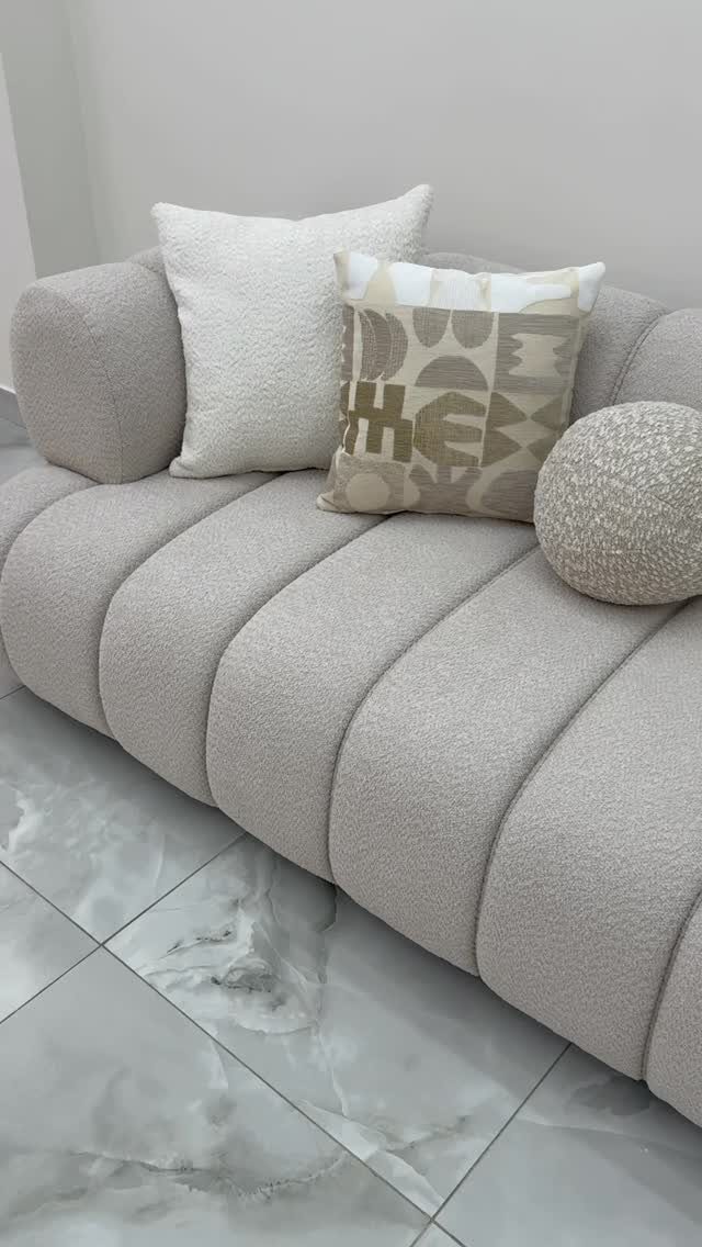 Light grey bouclé sofa with ribbed design and white decorative pillows on marble floor