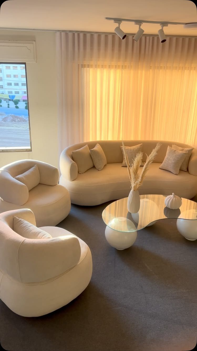 Curved cream sofa and rounded armchairs in a modern living room with glass table.