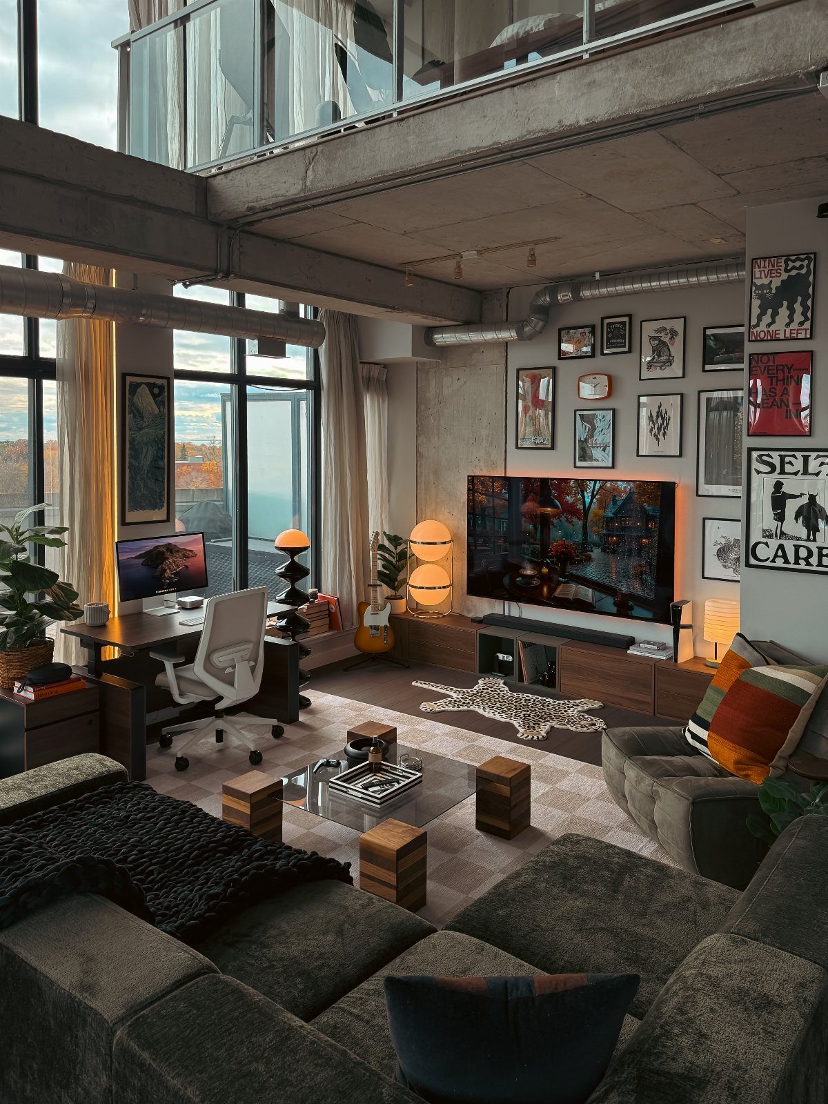 Modern industrial loft office with a grey couch, wooden desk, and gallery wall.