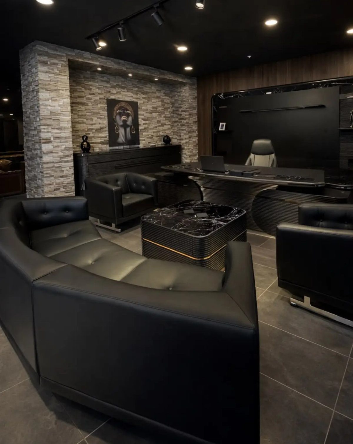 Modern office interior with black leather furniture, a large desk, and stone wall.