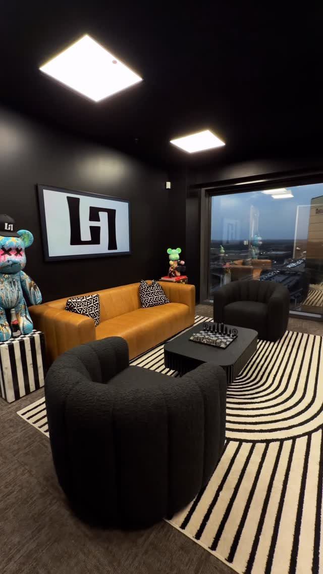 Modern office lounge with black walls, black armchairs, and a tan leather sofa.