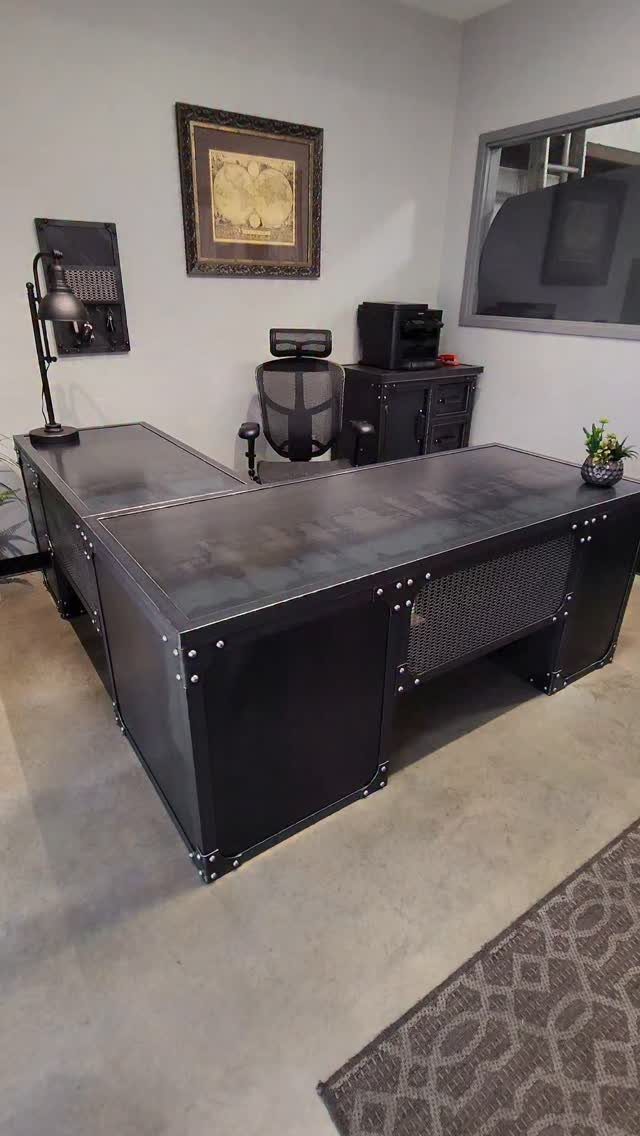 L-shaped black metal industrial desk with a black mesh chair in a grey office.