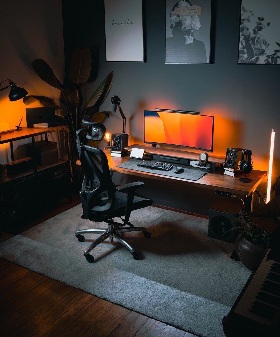 Home office desk with warm orange ambient lighting, black chair, and dark walls