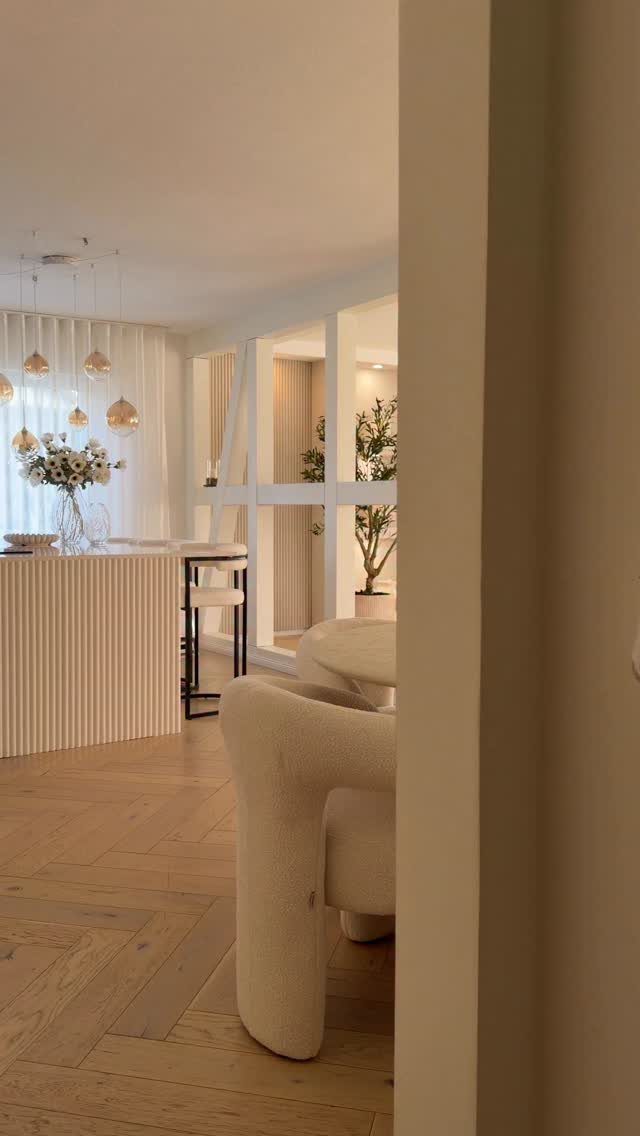 Curved white bouclé armchair in a bright, modern room with herringbone wood floors.
