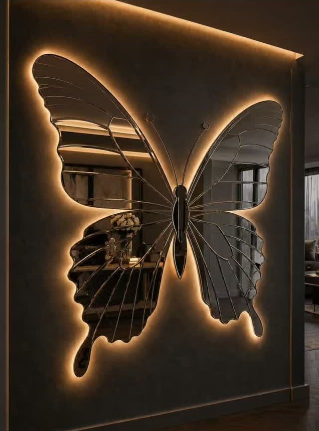 Butterfly-shaped mirror with warm backlight glowing against a dark grey interior wall