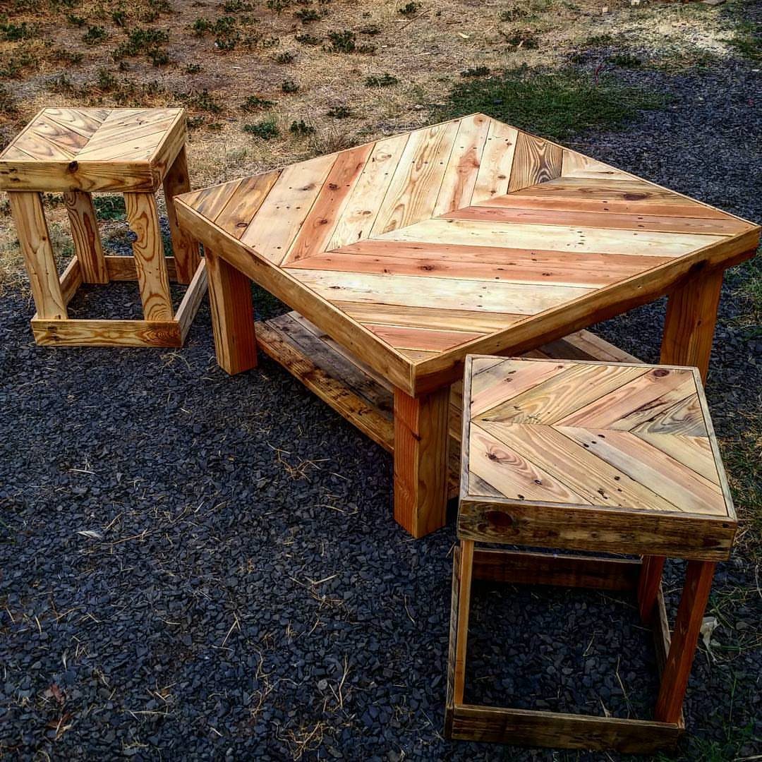 Chevron pattern pallet wood coffee table with two matching wooden stools on gravel.